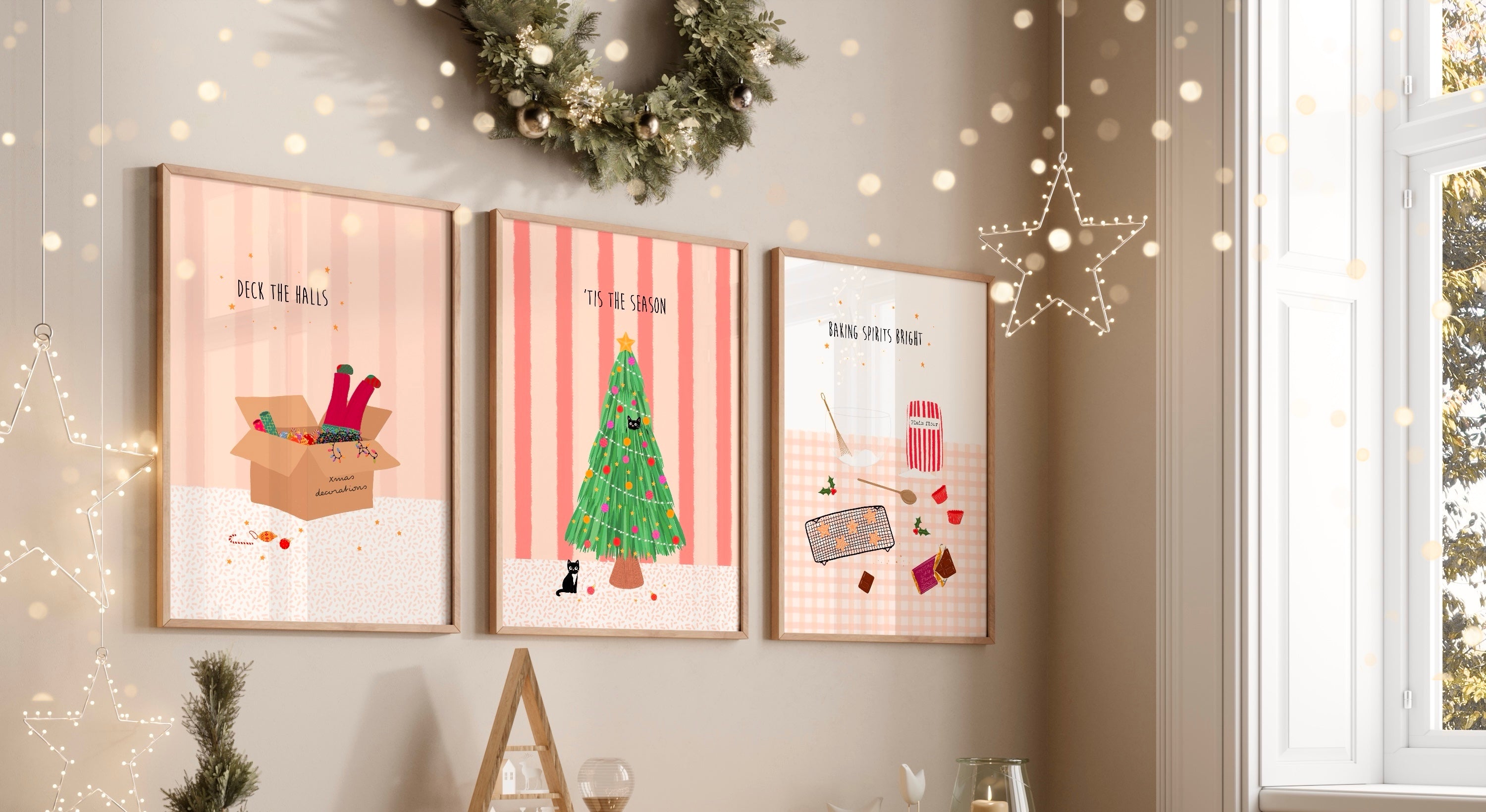 Three framed pink Christmas-themed prints on a wall with decorative lights and a window in the background