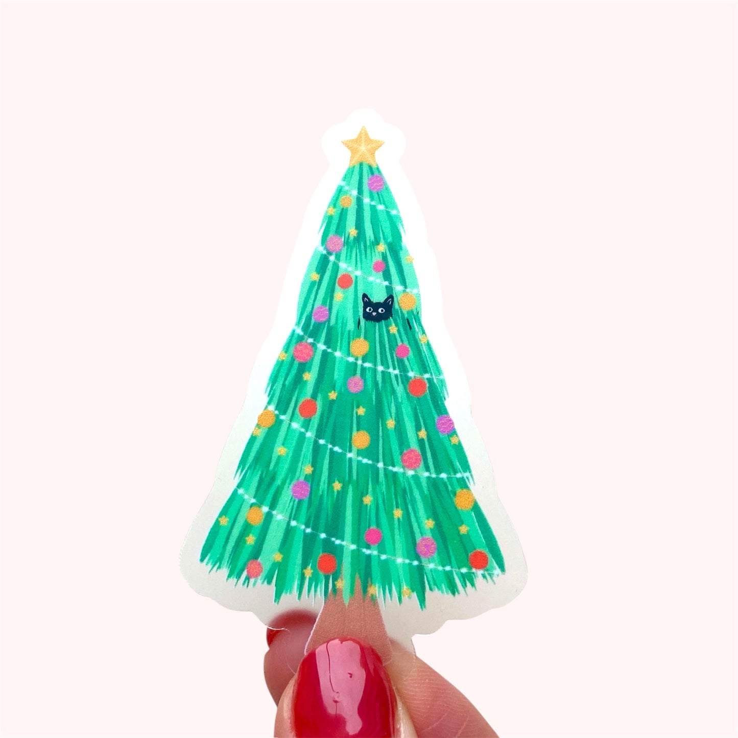 Decorative Christmas tree sticker with colourful ornaments and a star, with 2 black cats playing in and around the tree. Held up against a pink background.