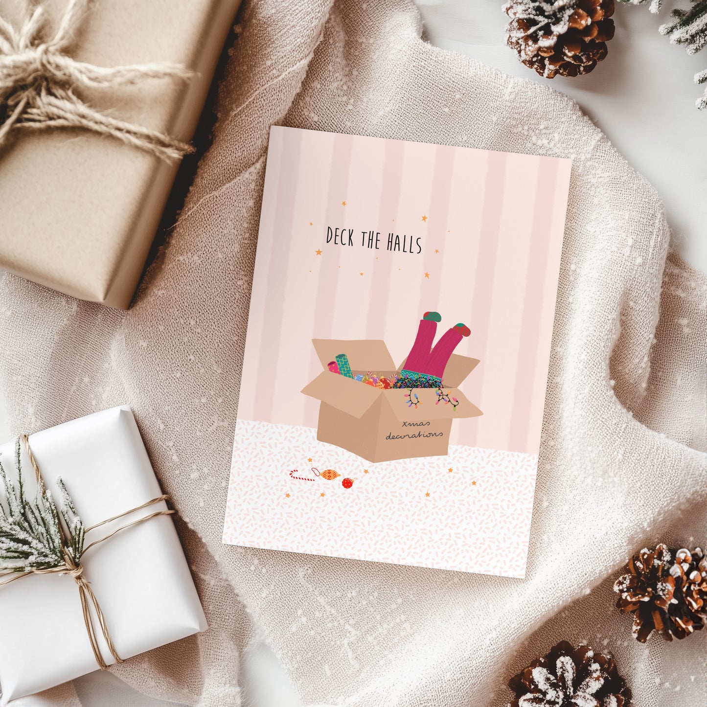 Christmas card with 'Deck the Halls' text and illustrations, surrounded by wrapped gifts and pine cones.