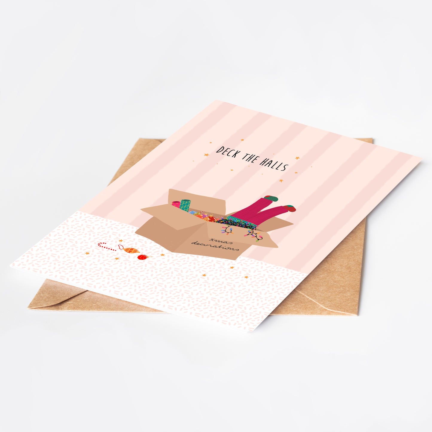 Pink striped greeting card with 'Deck the Halls' text and illustration of pink-trousered legs sticking out of a box of Christmas decorations and lights, with a brown kraft envelope