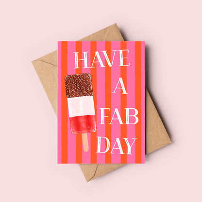 A greeting card with a pink and orange striped background, featuring an ice lolly  illustration and the text 'HAVE A FAB DAY' in white. The card is displayed on top of a brown kraft envelope against a solid pale pink background.