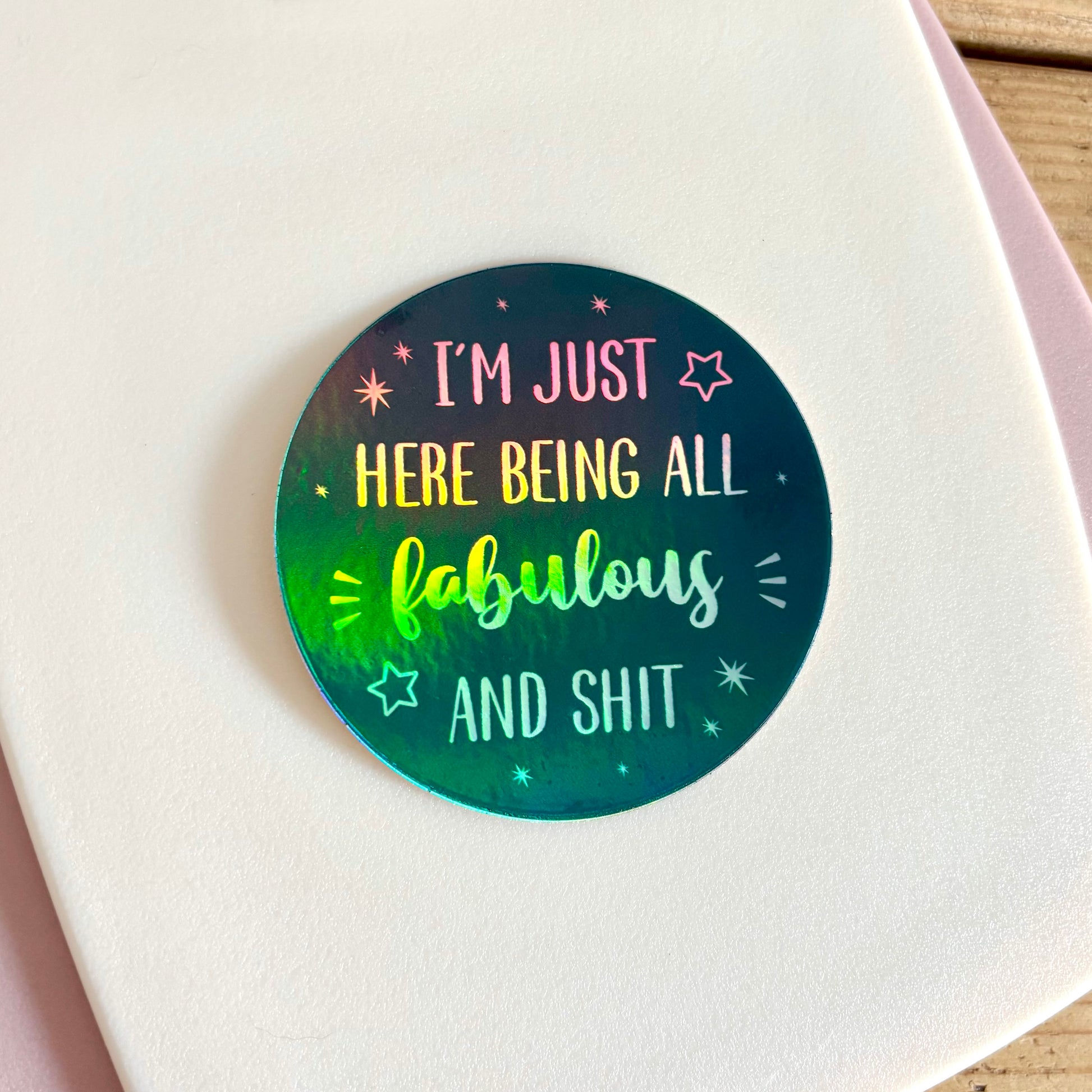 A round sticker with a holographic navy background and the text 'I'M JUST HERE BEING ALL fabulous AND SHIT', shown on a white card.