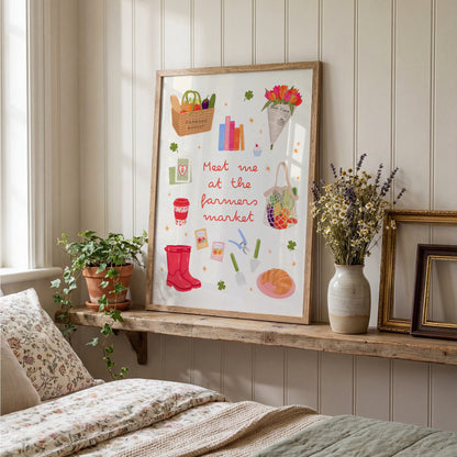 A framed art print featuring a whimsical 'Meet me at the farmers market' illustration with red rain boots, flowers, and market items, styled on a wooden shelf in a cozy bedroom setting.