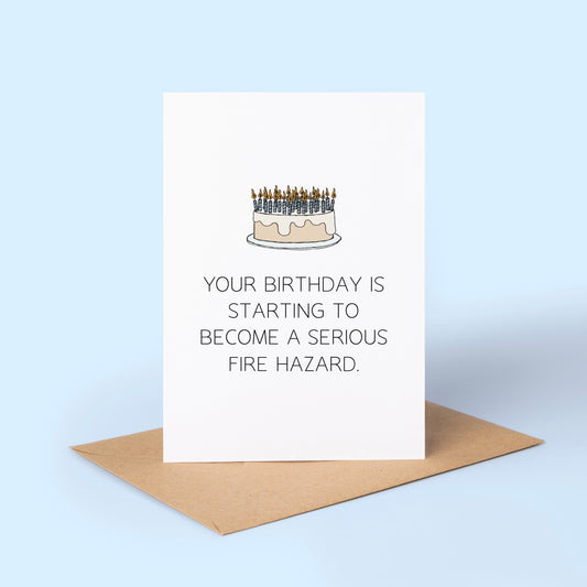 Birthday card with a cake illustration covered in candles and humorous fire hazard text on a light blue background