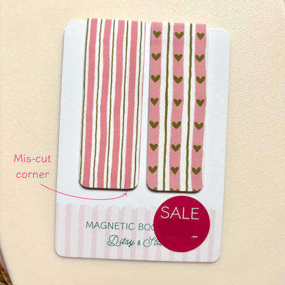 A white card holding two decorative rectangular magnetic pieces with pink and olive-green striping and heart motifs, photographed on a beige surface. Pink text reads 'Mis-cut corner,' and a magenta 'SALE' sticker is overlaid near the bottom.