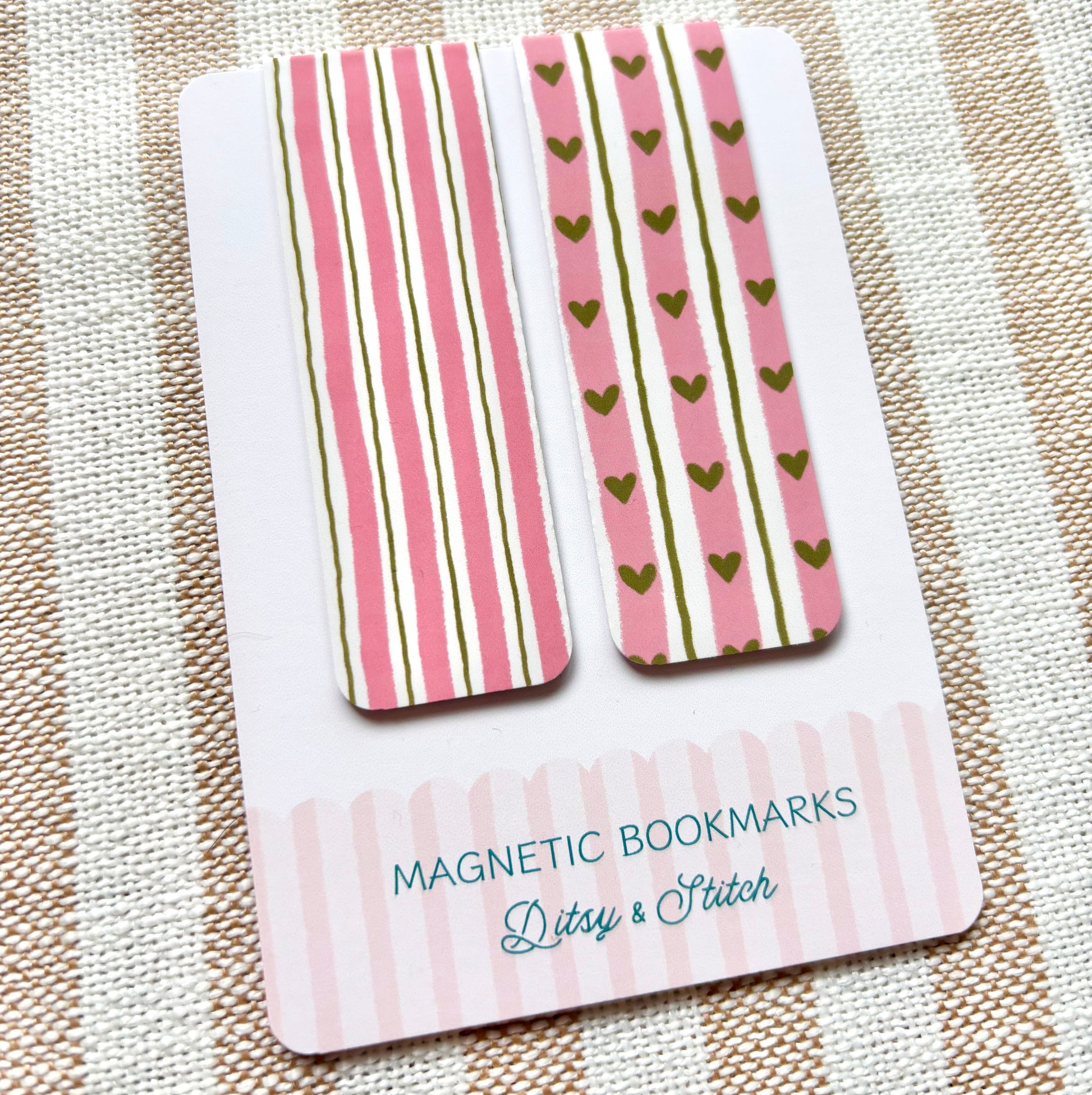 Two magnetic bookmarks with pink and green heart and striped patterns on a striped fabric background
