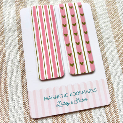 Two magnetic bookmarks with pink and green heart and striped patterns on a striped fabric background