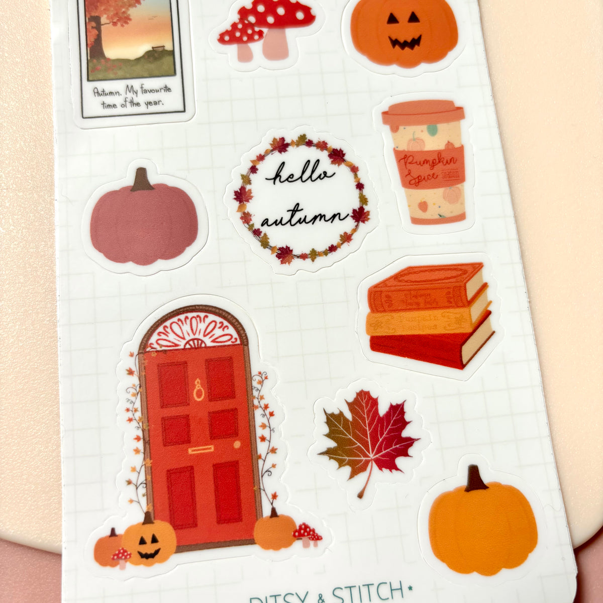 A sheet of autumn-themed planner stickers on a white grid background, featuring pumpkins, a red door, fall leaves, a mushroom, a coffee cup labeled pumpkin spice, books, and a 'hello autumn' wreath.