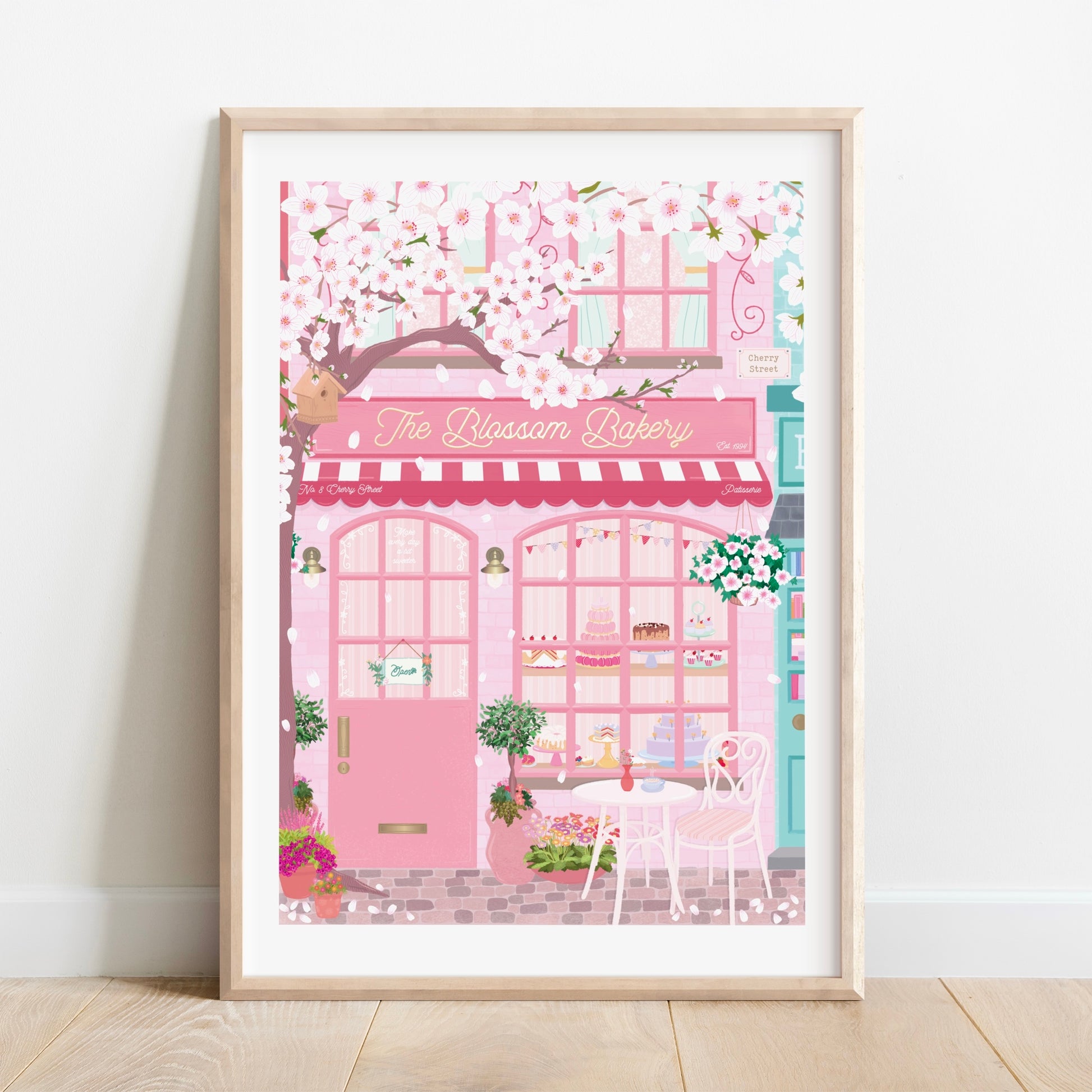 Framed illustration of a pink bakery named 'The Blossom Bakery' on a white wall.