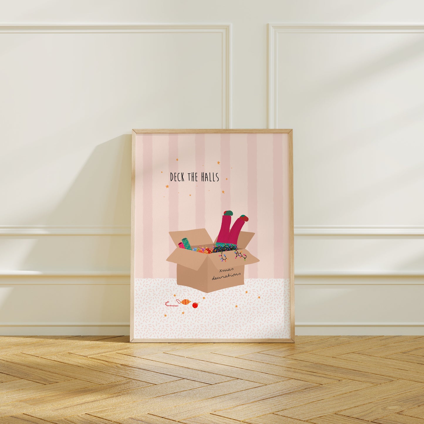 A pink striped illustration with a box of Christmas decorations and colourful lights and a girls legs in pink trousers and mismatched socks dangling out of the top