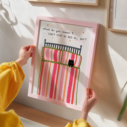 Person holding a framed illustration of a cat on a striped bed with text.