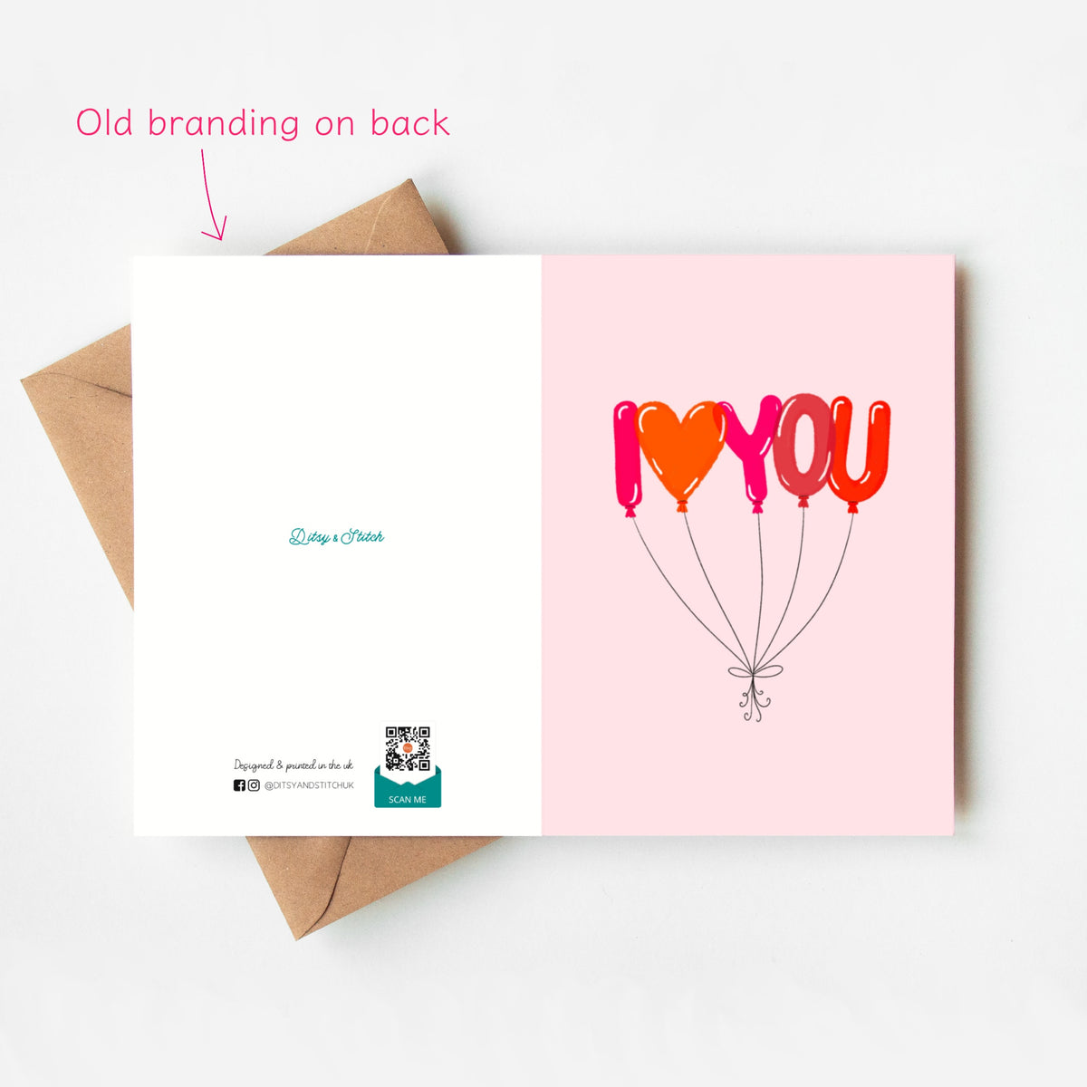 An open greeting card displayed on top of a brown envelope against a white background. The front shows a pink panel with the word 'I LOVE YOU' formed by balloon shapes in red, orange, and pink.