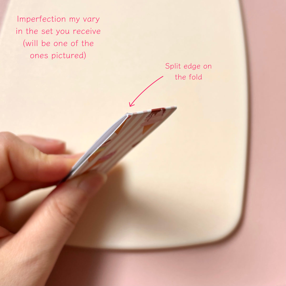 A hand holds a magnetic bookmark showing a split edge, with pink text callouts explaining that imperfections vary by set and pointing to the split edge on the fold. The background is a soft pink surface.