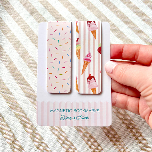 Hand holding a set of magnetic bookmarks with ice cream and sprinkles designs on a striped fabric background