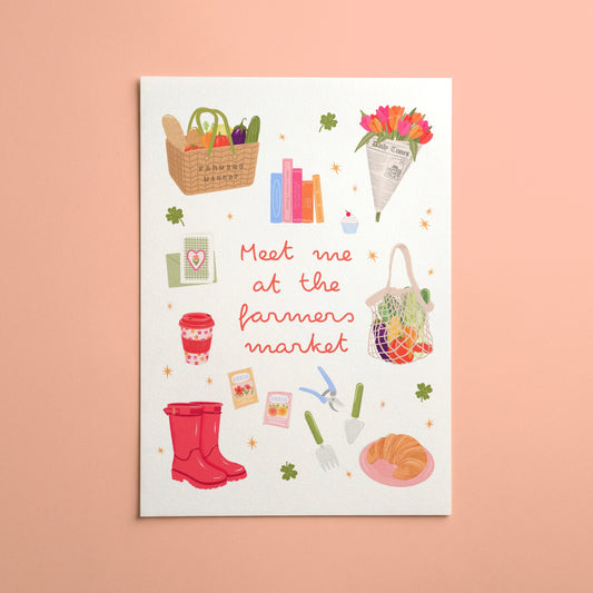 A white art print featuring a whimsical illustration of farm market items and the text 'Meet me at the farmers market' in red script, displayed against a solid peach-pink background.