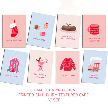 Eight Christmas-themed greeting cards arranged in two rows on a white background, with text below reading '8 HAND-DRAWN DESIGNS PRINTED ON LUXURY TEXTURED CARD A7 SIZE'. The cards feature pastel backgrounds and whimsical holiday illustrations including a stocking, a yule log, a cosy mug, a snowy pink house, a candy cane cocktail, a christmas jumper, and a train.
