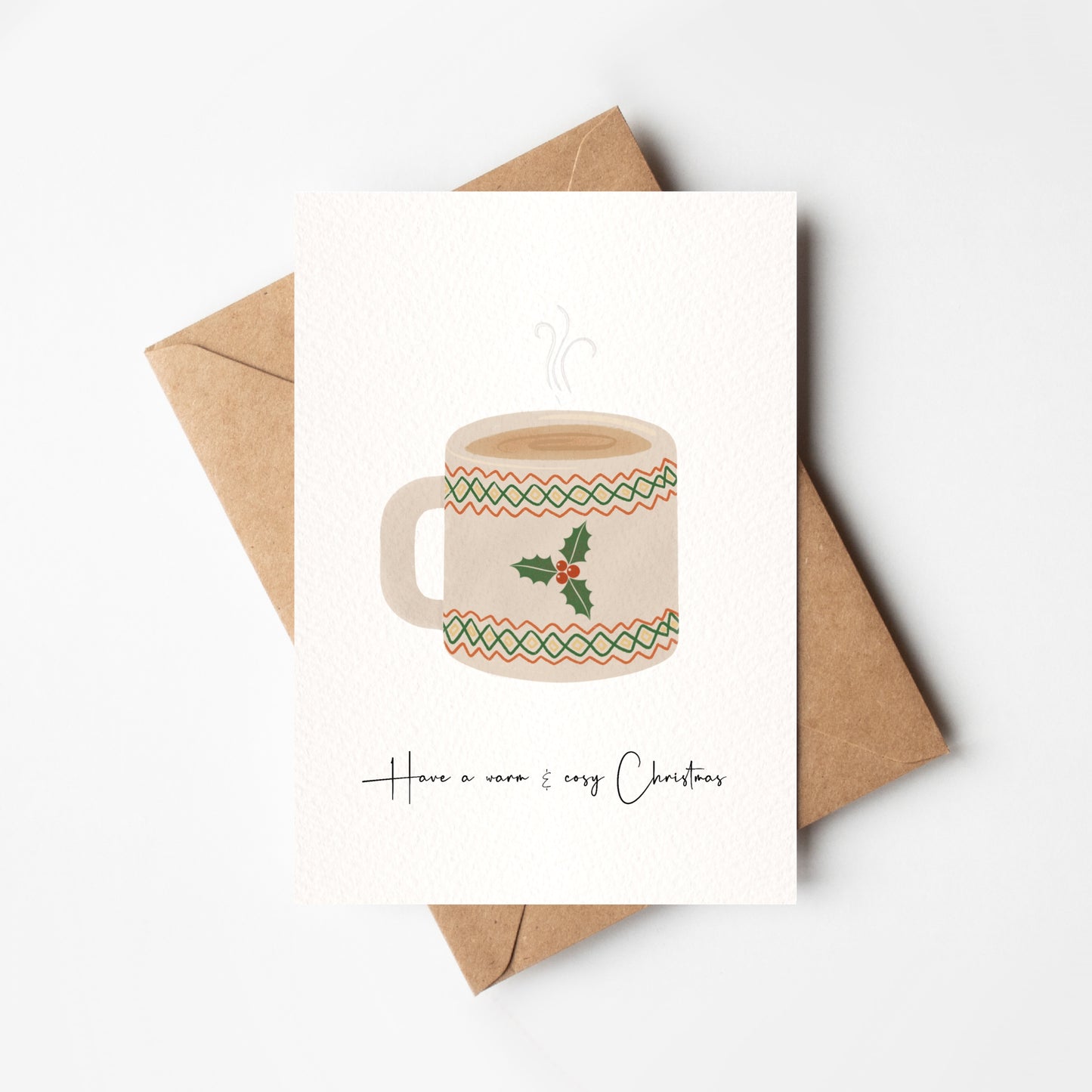 Card with a mug illustration and 'Have a warm & cozy Christmas' text, placed on a white background with a brown envelope.