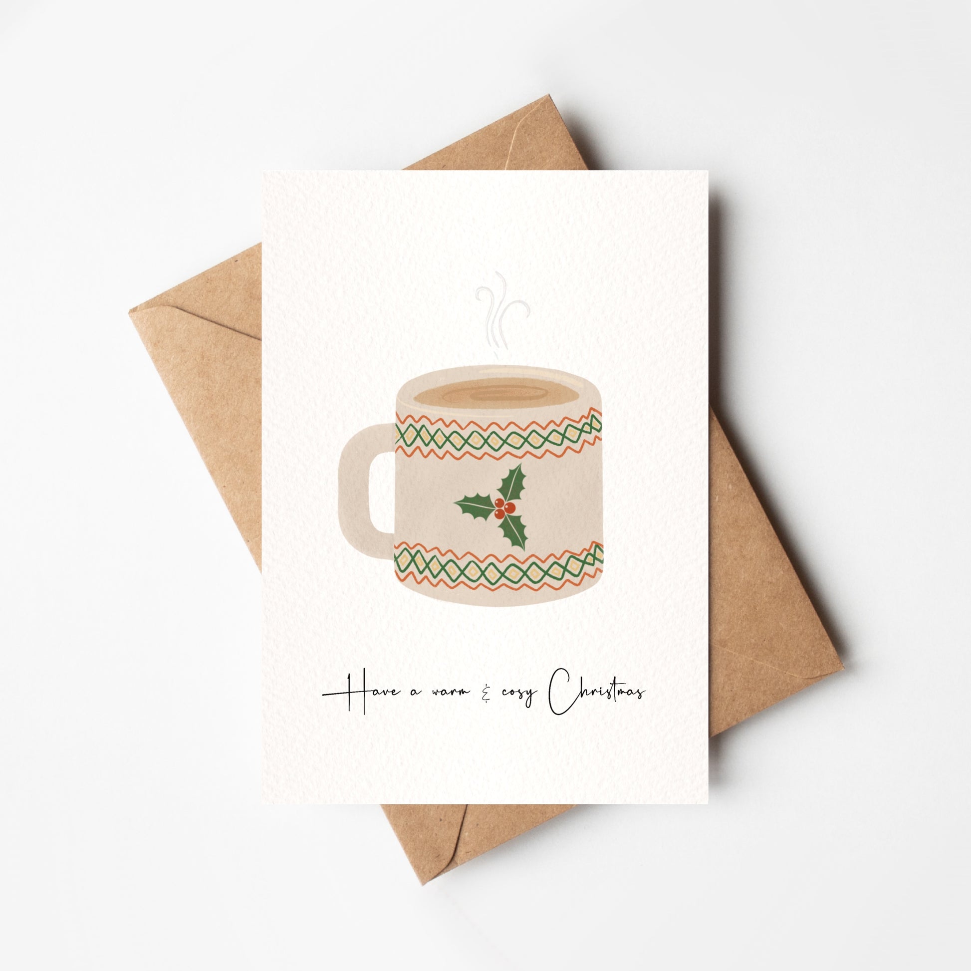 Card with a mug illustration and 'Have a warm & cozy Christmas' text, placed on a white background with a brown envelope.