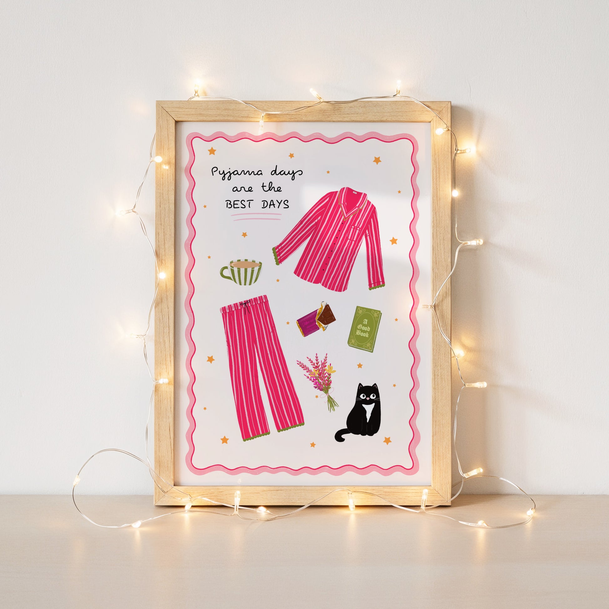Framed artwork with pink pyjama illustration and text 'Pyjama days are the BEST DAYS' on a white background surrounded by fairy lights.