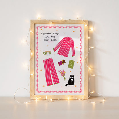 Framed artwork with pink pyjama illustration and text 'Pyjama days are the BEST DAYS' on a white background surrounded by fairy lights.