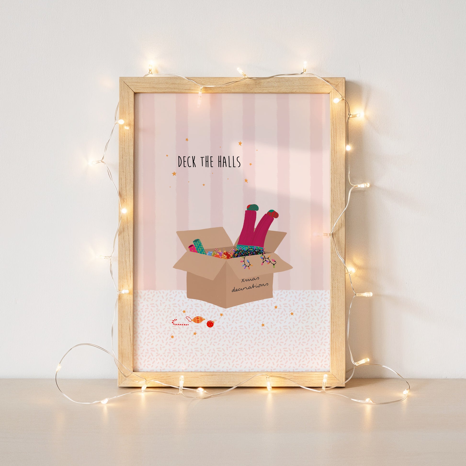 A pink striped illustration with a box of Christmas decorations and colourful lights and a girls legs in pink trousers and mismatched socks dangling out of the top