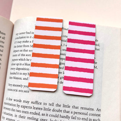 Two striped paper bookmarks, one with orange and white stripes and the other with pink and white stripes, placed on open book pages.