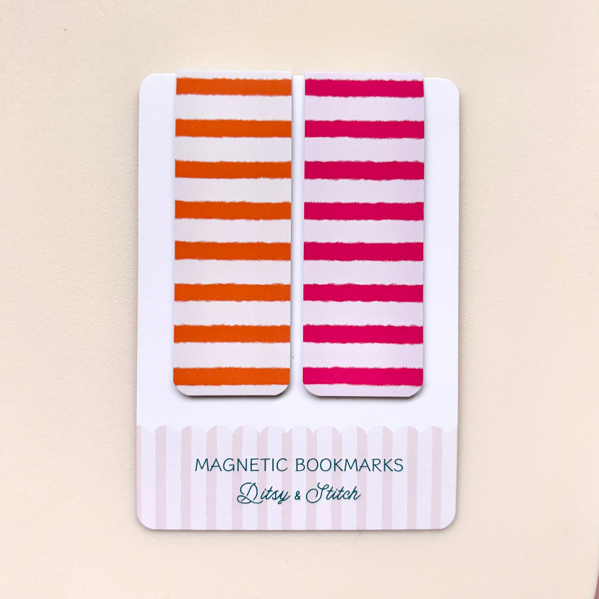 Two rectangular magnetic bookmarks with horizontal striped patterns, one in orange and white and the other in pink and white, displayed on a white backing card labeled 'MAGNETIC BOOKMARKS Ditsy & Stitch' against a light beige background.