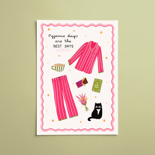 A vertical art print featuring a whimsical illustration of pink striped pajamas and matching pajama pants, surrounded by cozy and playful elements like a mug, flowers, a black cat, and a passport. The text reads 'Pajama days are the BEST DAYS'.