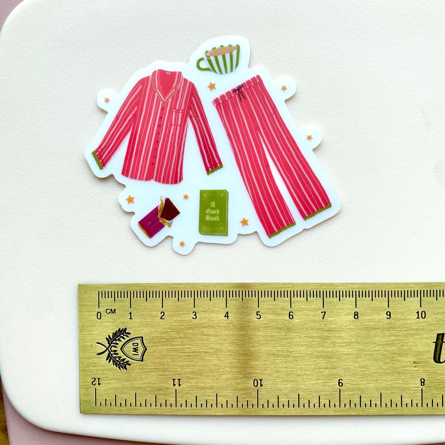 Sticker of pink striped pyjamas with accessories on a white background, next to a ruler for scale.