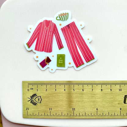 Sticker of pink striped pyjamas with accessories on a white background, next to a ruler for scale.