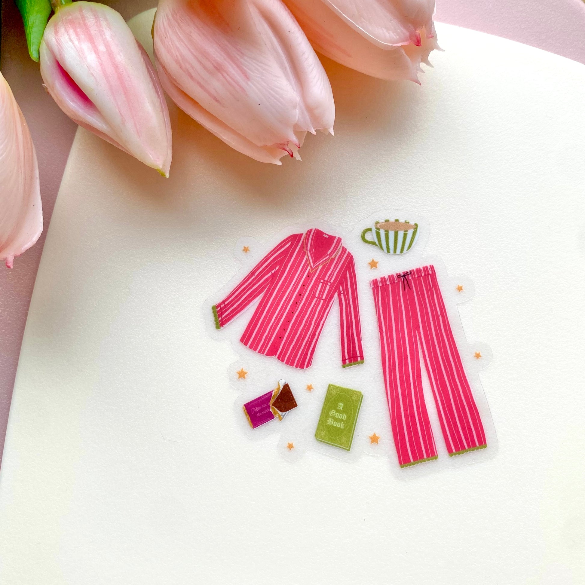 Pink striped pyjamas with cosy drink, book and chocolate on a white surface with pink tulips.