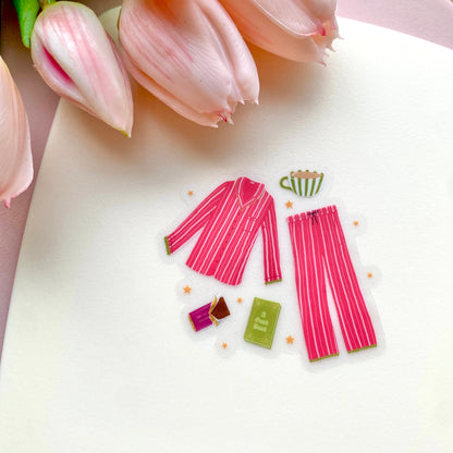 Pink striped pyjamas with cosy drink, book and chocolate on a white surface with pink tulips.