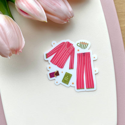 Sticker of a pink striped pyjama set with a book, mug and chocolate on a white surface with pink tulips.