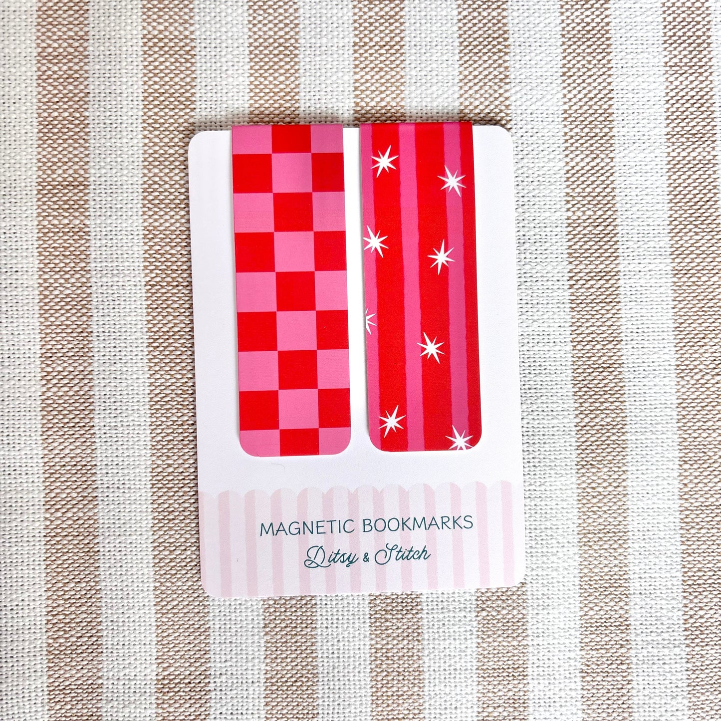Two red and pink checkered magnetic bookmarks on a striped fabric background