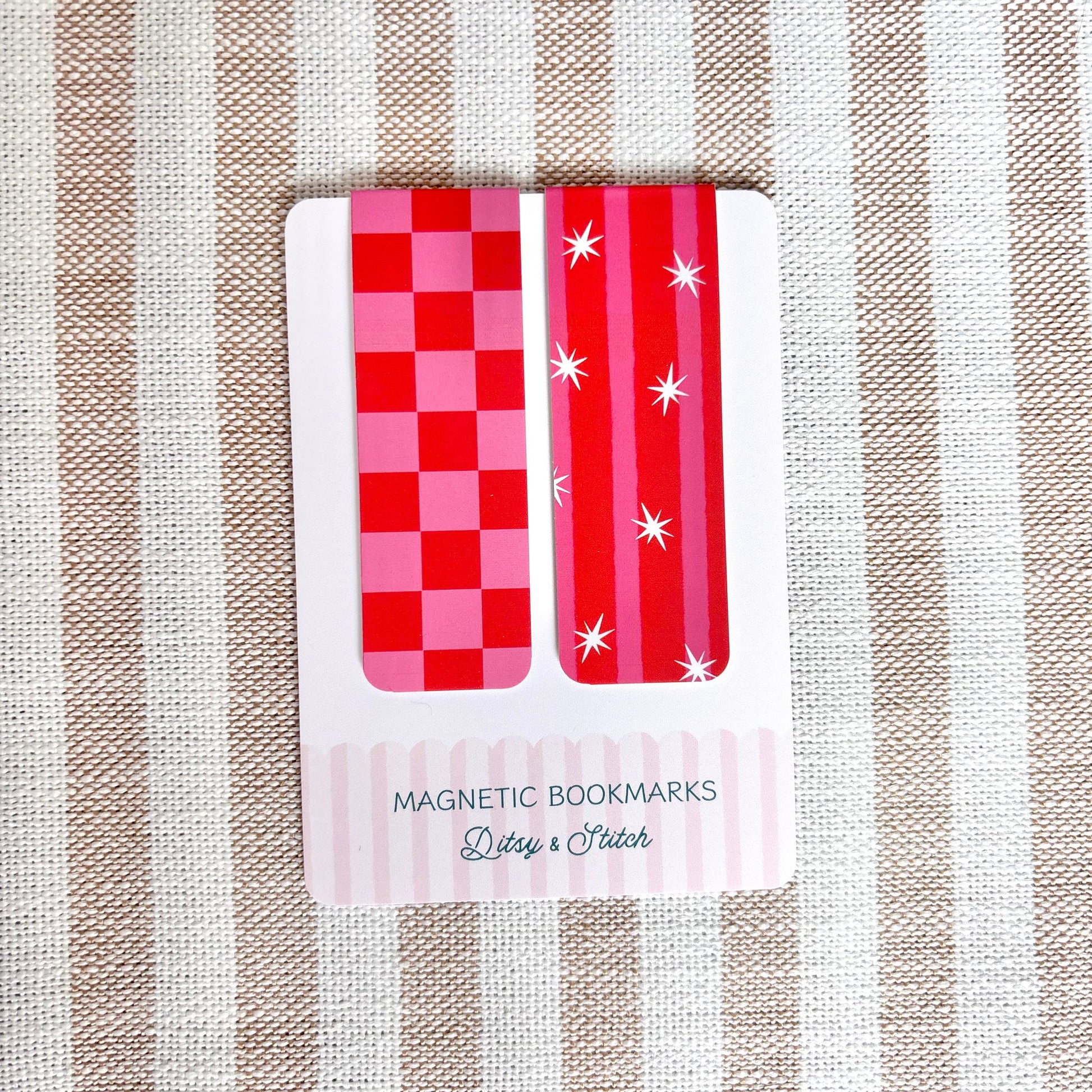 Two red and pink checkered magnetic bookmarks on a striped fabric background