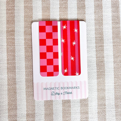Two red and pink checkered magnetic bookmarks on a striped fabric background