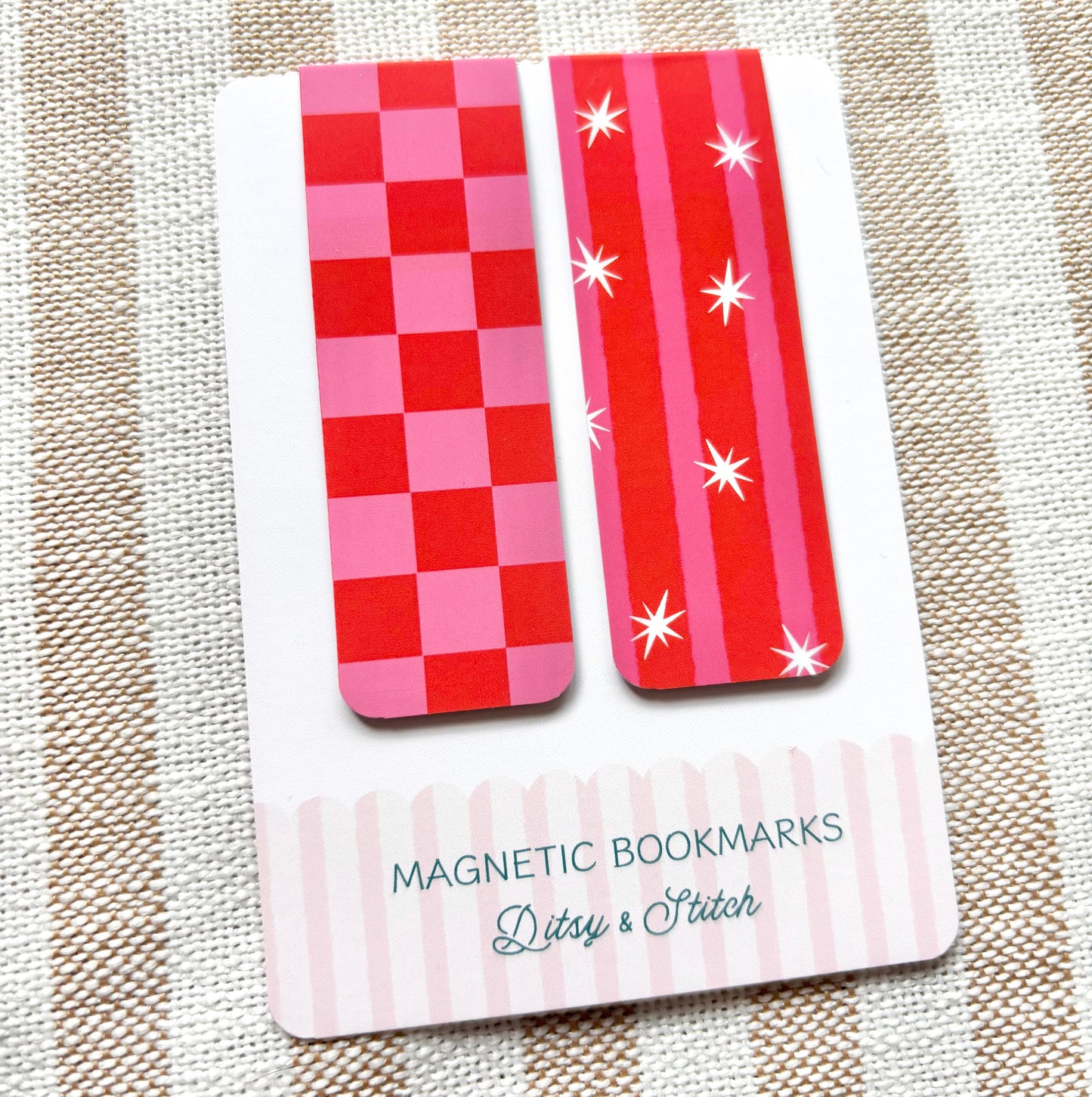 Two red and pink striped magnetic bookmarks on a card with 'Ditsy & Stitch' branding, placed on a striped fabric background.