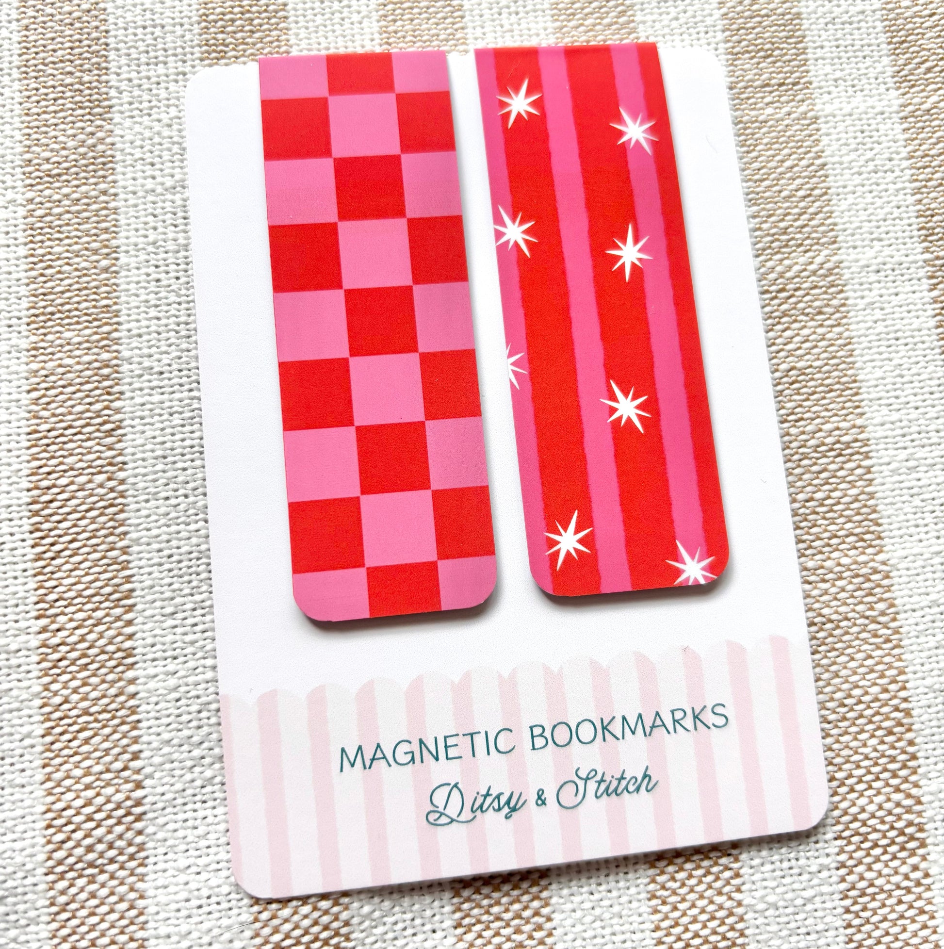 Two red and pink striped magnetic bookmarks on a card with 'Ditsy & Stitch' branding, placed on a striped fabric background.