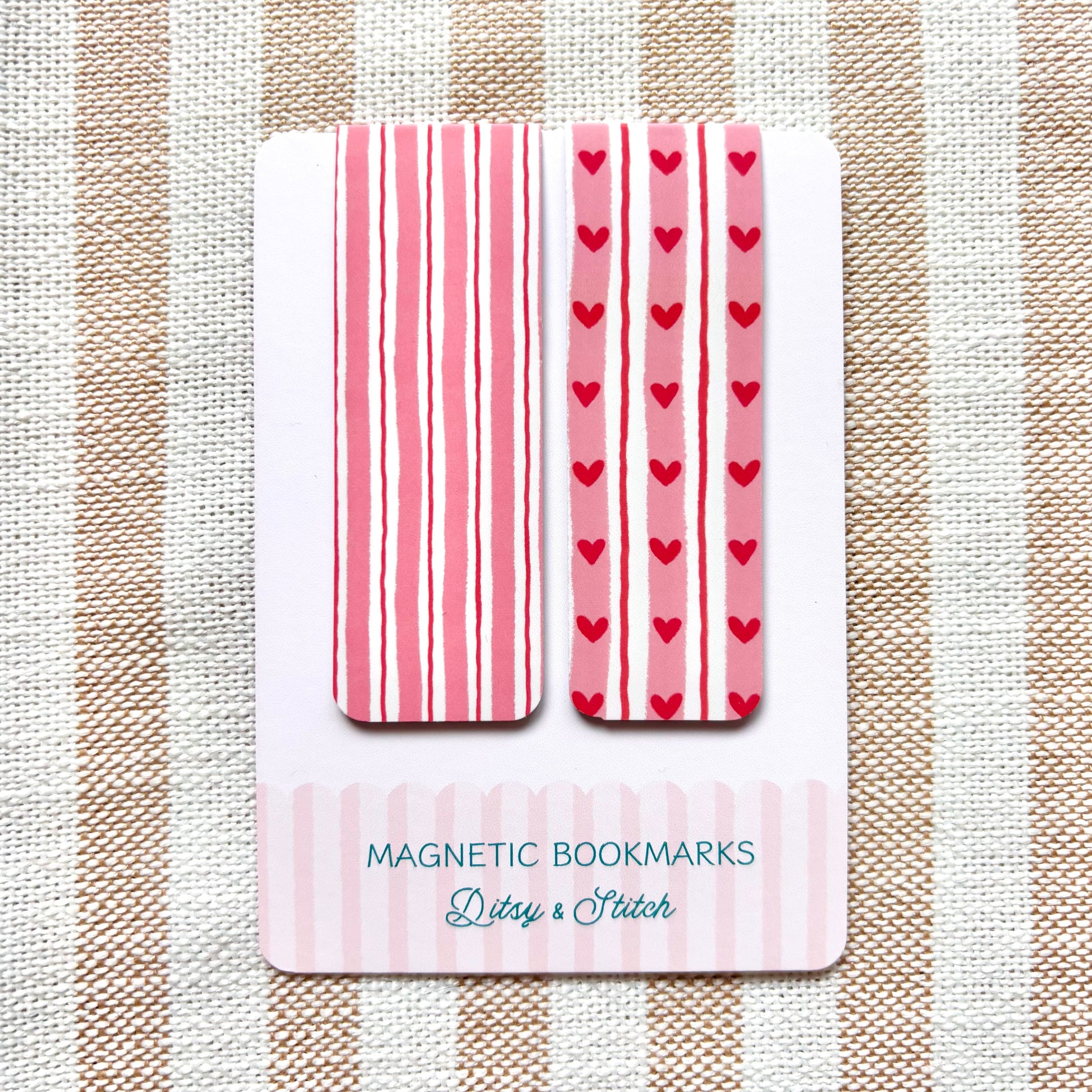 Set of magnetic bookmarks with pink stripes and red hearts on a striped fabric background