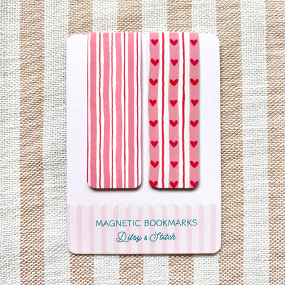 Set of magnetic bookmarks with pink stripes and red hearts on a striped fabric background