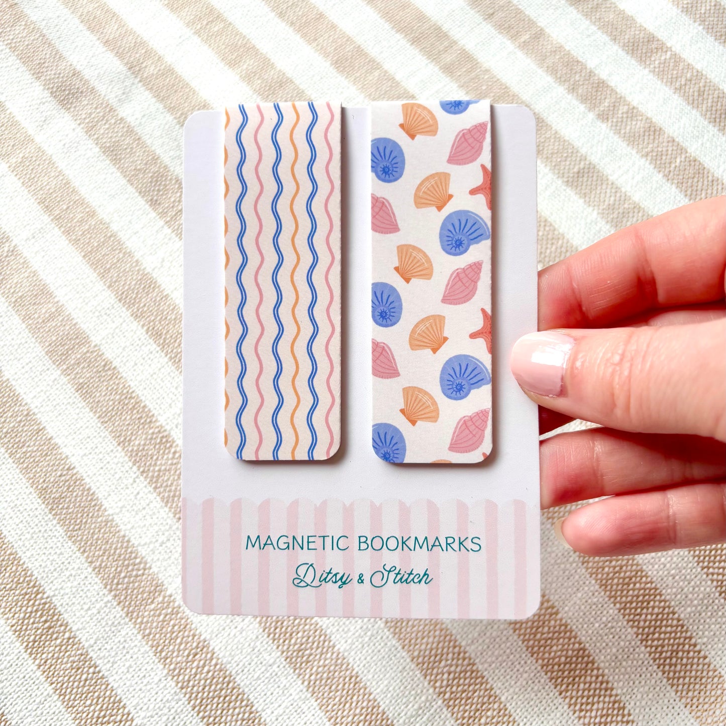 Two magnetic bookmarks with shell pattern design held by a hand on a striped background