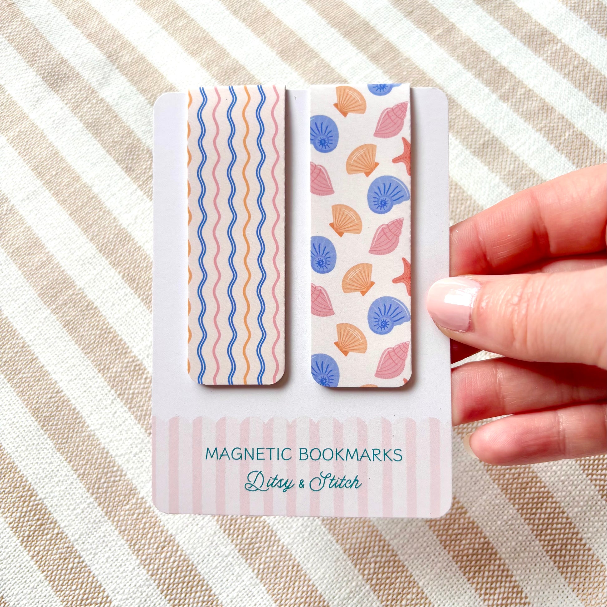 Two magnetic bookmarks with shell pattern design held by a hand on a striped background