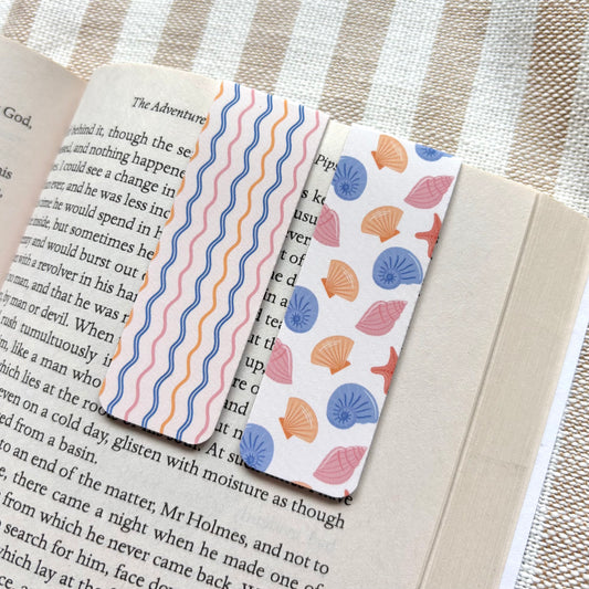 Two sea shell patterned bookmarks on an open book with a striped background