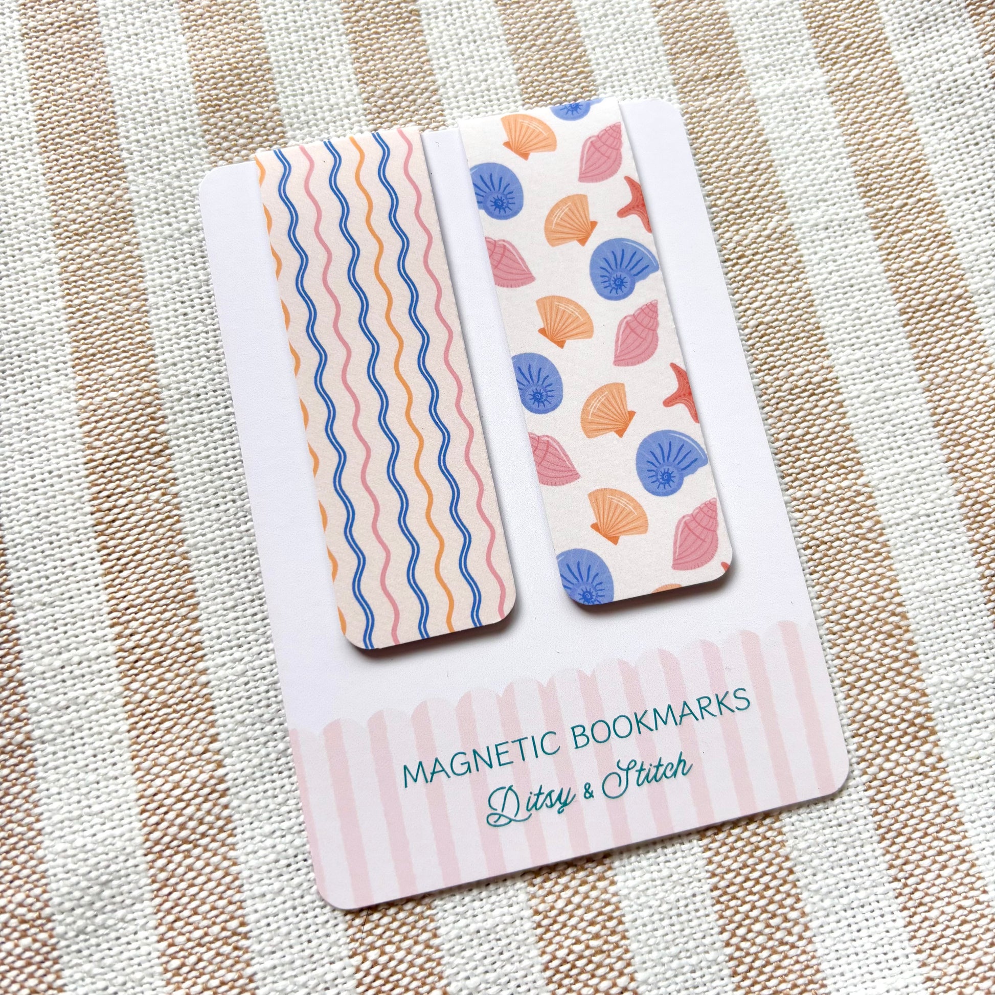 Two magnetic bookmarks with shell and wave patterns on a striped fabric background
