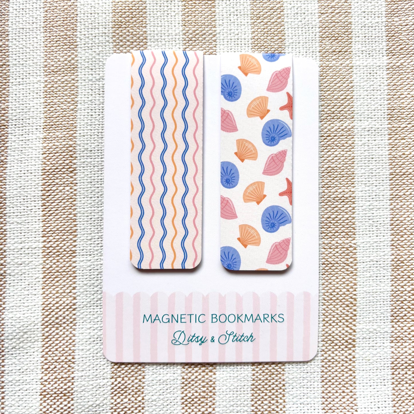 Two magnetic bookmarks with shell and wavy pattern designs on a striped fabric background.