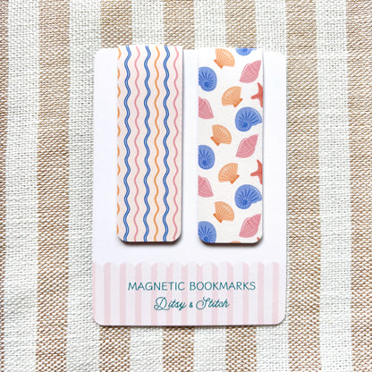 Two magnetic bookmarks with shell and wavy pattern designs on a striped fabric background.