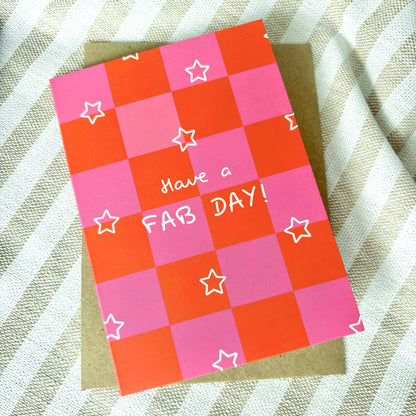 Checkered pink and orange greeting card with stars and 'Have a FAB DAY!' text on a textured fabric background