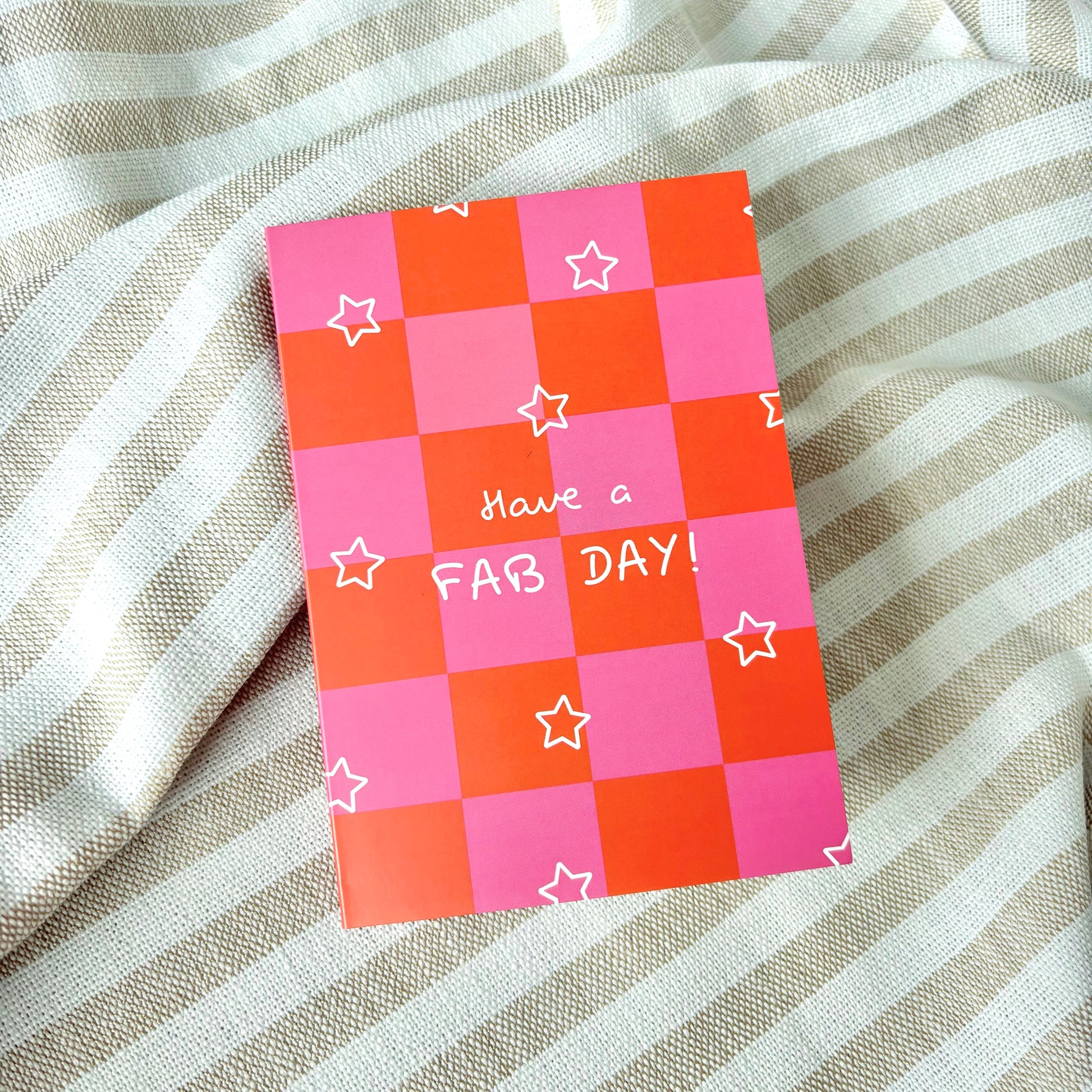 Checkered pink and orange greeting card with 'Have a FAB DAY!' text and white stars on a striped fabric background