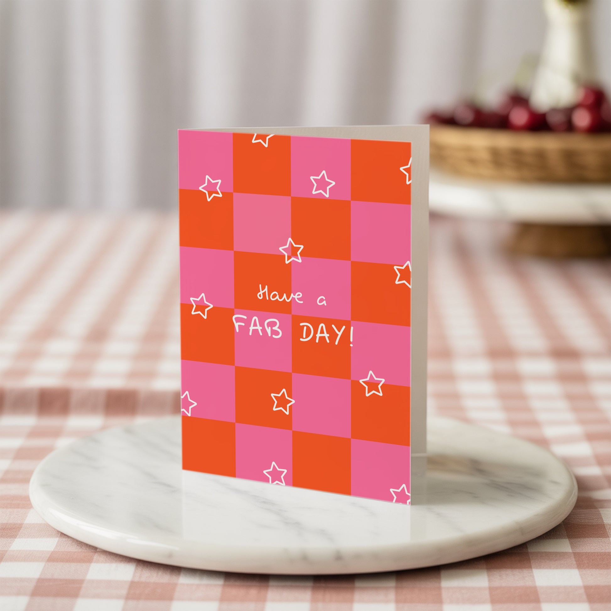 Greeting card with pink and orange checkered pattern and 'have a fab day' text and white stars on a marble stand.