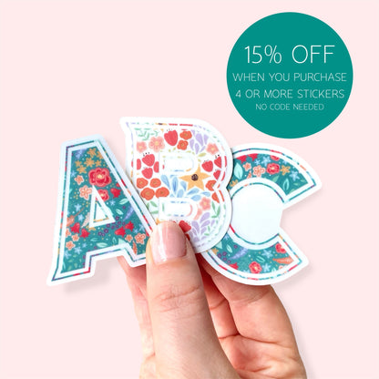 Hand holding floral-themed letter stickers with a promotional offer on a light pink background
